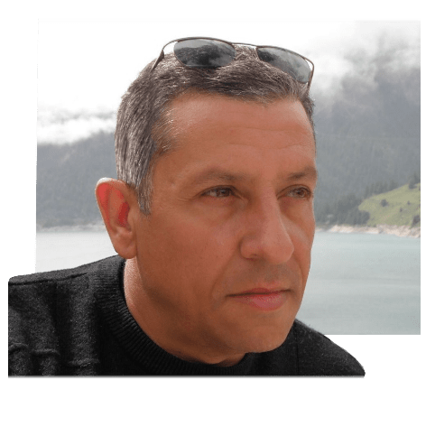 Portrait d'un homme avec des lunettes de soleil, regardant au loin, près d'un plan d'eau et avec une vue panoramique de montagnes en arrière-plan.