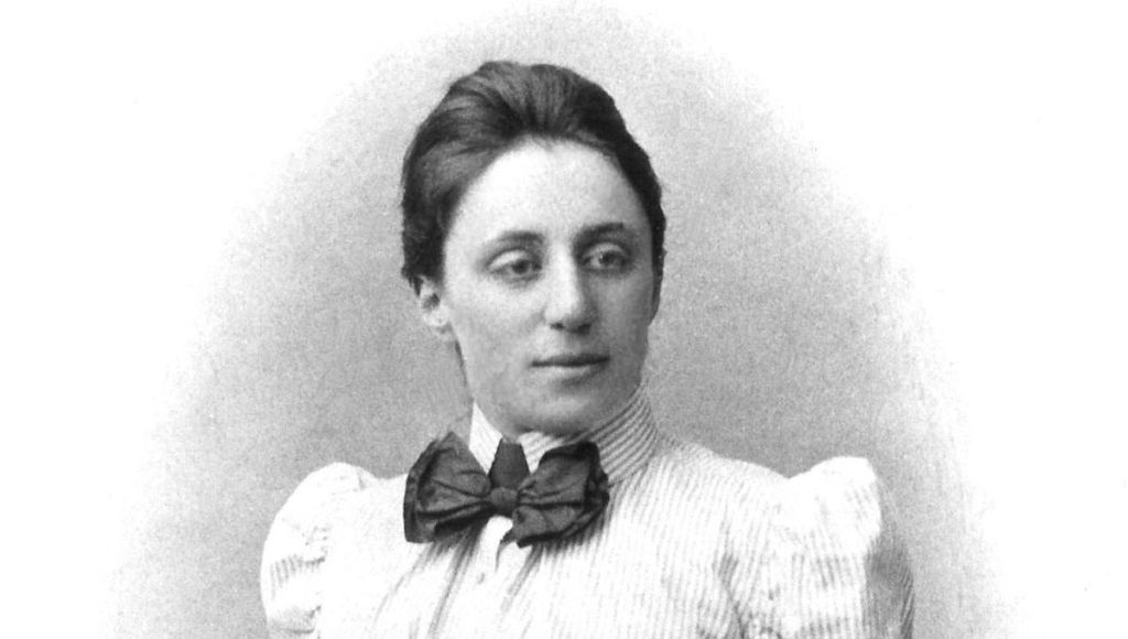 Portrait d'une femme en costume victorien avec un nœud papillon, regard sérieux, fond clair.